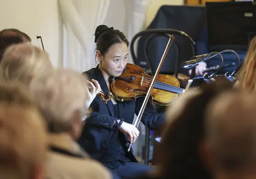 Nahaufnahme einer Violinistin inmitten des Orchesters.