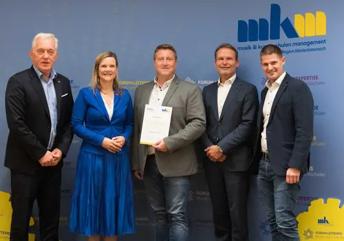 Gruppenfoto von fünf Personen nebeneinander. Die Person in der Mitte hält ein Dokument und ist der 200. Absolvent der Akademie.