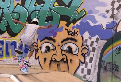 ein Skateboarder turnt vor einer Graffitiwand