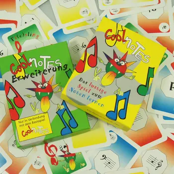 Das gelbe Basisspiel „Cool Notes“ und die grüne Erweiterung liegen auf einer Fläche voller einzelner Spielkarten.