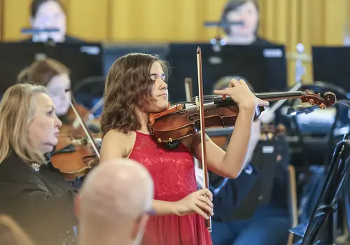 Ein Mädchen spielt auf ihrer Geige umgeben von einem Orchester.