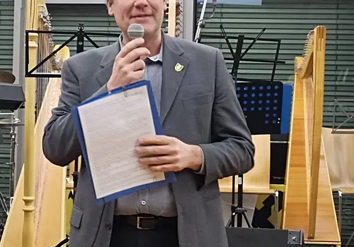 Eine Person moderiert den Abend und hält ein Mikrofon und einen Zettel in den Händen.