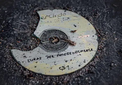 Eine zerbrochene CD liegt auf einem schmutzigen Boden. Auf der CD steht handgeschrieben „Lukas der Ameisenschreck“.