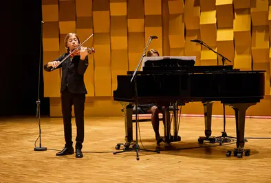 Ein Junge spielt auf der Bühne Geige, begleitet von einer Pianistin.