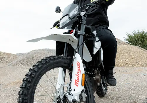 Ein Motorradfahrer sitzt auf seinem Motorrad, aus einer niedrigen Perspektive aufgenommen. Das Vorderrad ist dabei im Fokus.