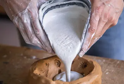 Eine Person kippt Modelliergips in eine, selbst aus Ton geformte, Schüssel.