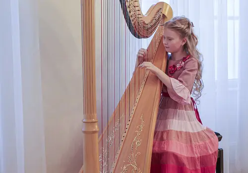 in Mädchen posiert in einem langen, rosafarbenen Kleid neben ihrer Harfe.