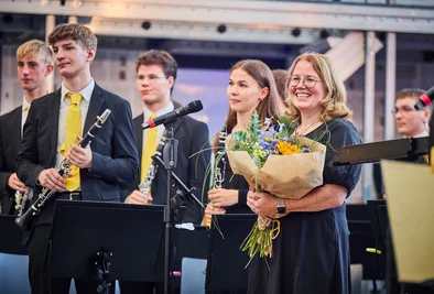Moderation mit Blumenstrauße, daneben Klarinettisten