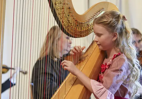 Ein Mädchen spielt ein Stück auf einer Harfe umgeben von einem Orchester. 