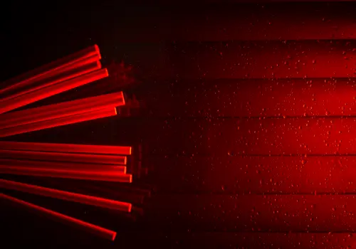 Glaswand mit Wassertröpfchen. Von links ragen mehrere Stäbe ins Bild, während rotes Licht von rechts einfällt.