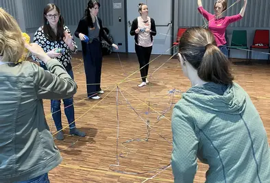 Personen stehen im Kreis und in der Mitte haben sie Wolle gespannt.