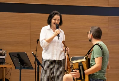 Frau mit Mikrofon im Gespräch mit einem Mann, der ein Akkordeon hält.