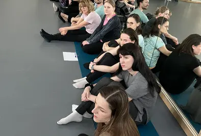 Teilnehmende sitzen an der Wand aufgereiht auf dem Boden.