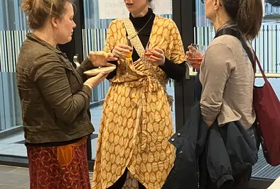 Drei Frauen sprechen miteinander während sie Getränke und Essen in den Händen halten.