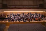 Gruppenfoto des Jugendsinfonieorchesters auf der Bühne eines Konzertsaals.