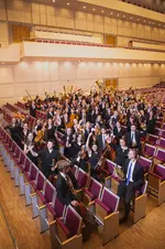 Gruppenfoto des Jugendsinfonieorchesters zwischen den Sitzreihen eines Konzertsaals.