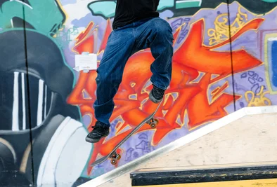 ein Skateboarder turnt vor einer Graffitiwand