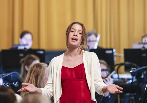 Eine Jugendliche singt umgeben von einem Orchester.