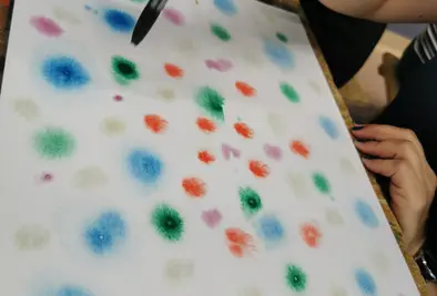 Eine Person malt mit einem Pinsel bunte Punkte auf Papier.