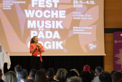 Person auf der Bühne vor einer Präsentationsfolie mit dem Schriftzug „Festwoche Musikpädagogik“.
