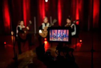 Eine Kamera filmt ein Gitarrenensemble auf einer rot beleuchteten Bühne.