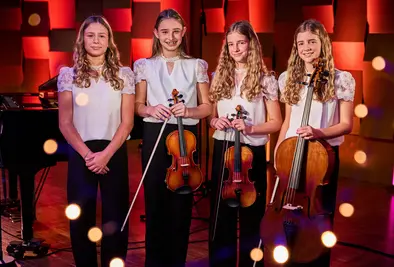 Vier Mädchen stehen auf einer Bühne und halten Streichinstrumente.