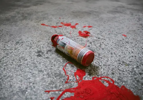 Eine Tube mit roter Farbe liegt auf einem Steinboden, umgeben von mehreren roten Farbflecken.