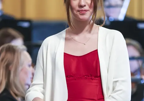 Eine Jugendliche singt umgeben von einem Orchester.