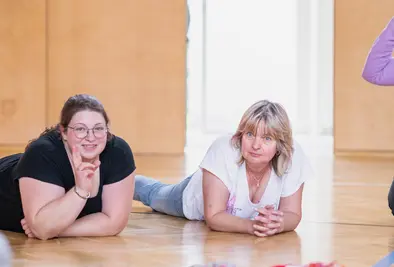Zwei Personen liegen auf dem Bauch und vor ihnen liegen mehrere Wollknäuel.