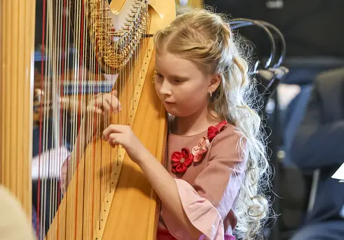 Ein Mädchen spielt ein Stück auf einer Harfe umgeben von einem Orchester. 