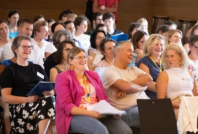 Teilnehmerinnen und Teilnehmer sitzen im Publikum und applaudieren.