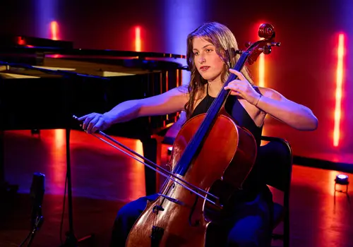 Eine Frau sitzt auf einem Sessel und spielt Kontrabass. Links im Hintergrund steht ein schwarzer Flügel, und rotes Licht sorgt für eine stimmungsvolle Atmosphäre.