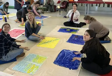Teilnehmende sitzen auf dem Boden und malen auf A3 Blättern mit ihren Händen.
