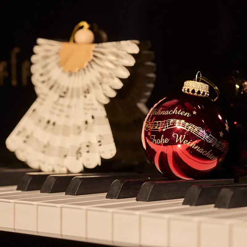 Papierengel und Weihnachtskugel liegen auf einem Klavier