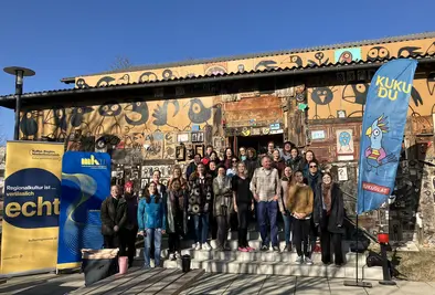 Gruppenfoto vor dem Gebäude mit vielen, simplen KUKUDU Illustrationen auf der Fassade