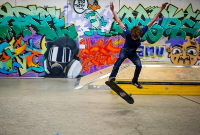 ein Skateboarder turnt vor einer Graffitiwand
