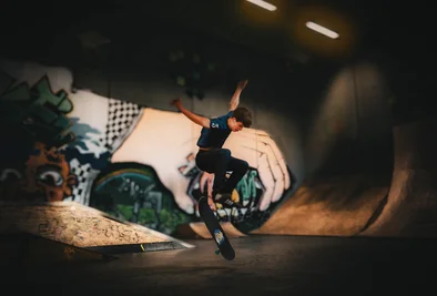 ein Skateboarder turnt vor einer Graffitiwand