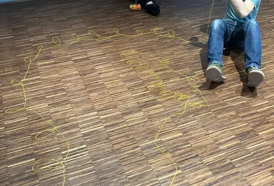 Zwei Personen sitzen am Boden und rollen jeweils ein Wollknäuel auf.