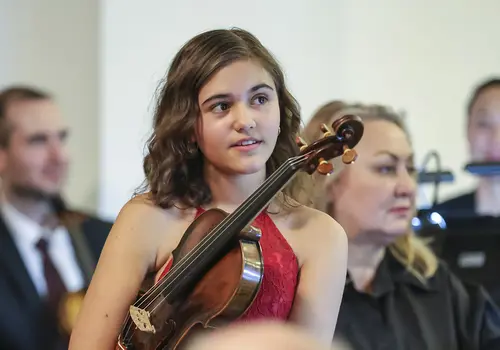 Ein Mädchen hat ihre Geige unter ihrer rechten Achsel eingeklemmt.