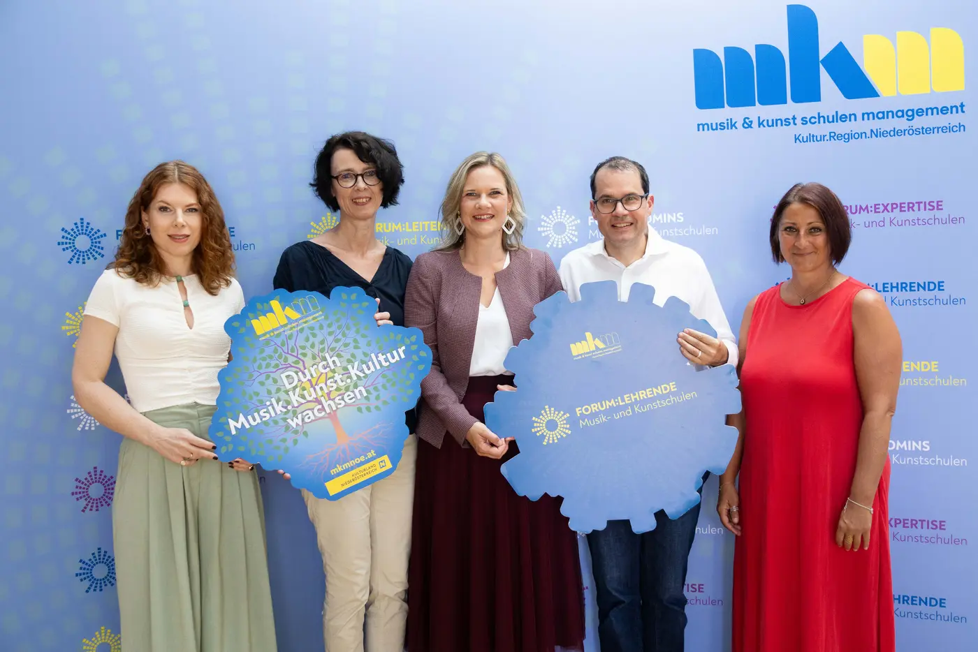 Gruppenfoto von fünf Personen mit zwei großen Logos in den Händen. 