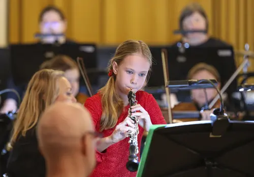 Ein Mädchen spielt auf ihrer Oboe umgeben von einem Orchester.