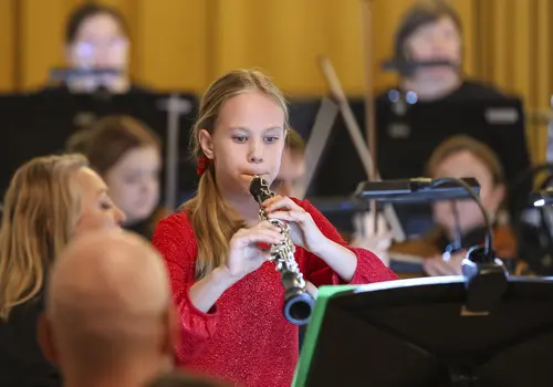 Ein Mädchen spielt auf ihrer Oboe umgeben von einem Orchester.
