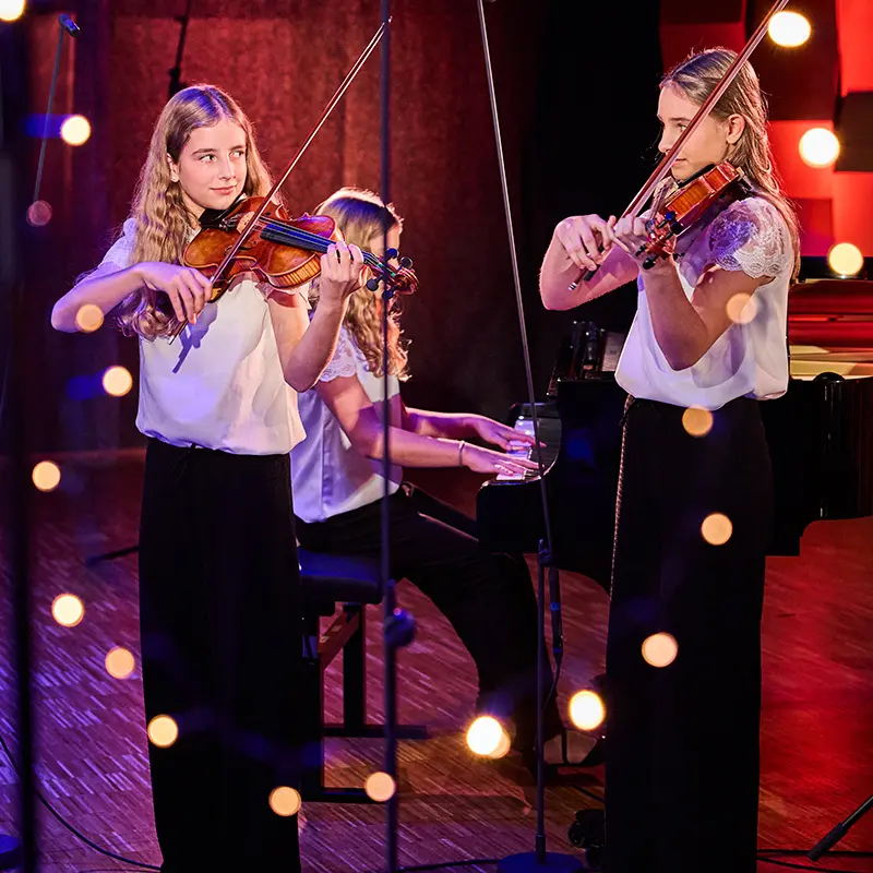 Zwei Mädchen spielen Geige umgeben von Lichtern.