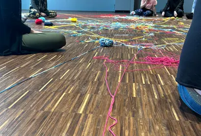 Teilnehmende sitzen am Boden und in der Mitte liegen teilweise aufgerollte Wollknäuel.