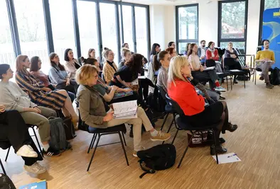 Teilnehmende sitzen in drei Reihen und sind auf die Präsentation fokussiert