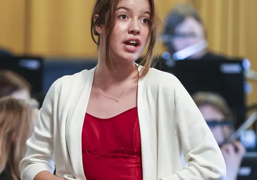 Eine Jugendliche singt umgeben von einem Orchester.