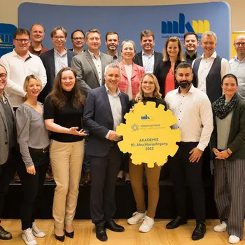 Gruppenfoto der 21 Absolventinnen und Absolventen der FORUM:LEITENDE Akademie. Eine Person hält ein großes Logo in der Hand.