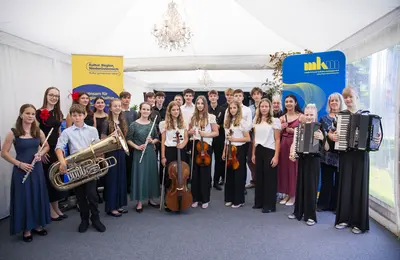Gruppenfoto der Musizierenden mit ihren Instrumenten. Im Hintergrund stehen MKM-Aufsteller.