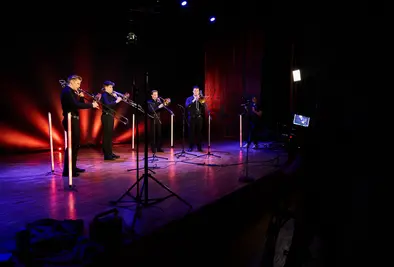 Vier Personen spielen auf einer Bühne Posaune und werden dabei von einem Kameramann gefilmt.