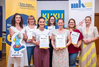 Teilnehmende Person und Vortragende posieren mit Zertifikat und KUKUDU Logo.